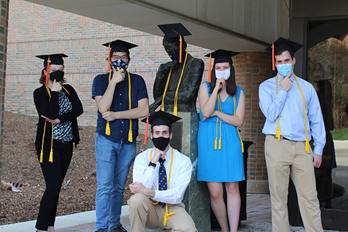group of masked students in grad cap and gown pose around the statue of Claude Shannon on North Campus