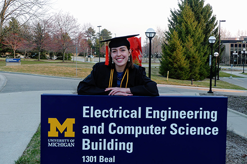 Gillian Minnehan in grad cap and gown behind EECS building sign